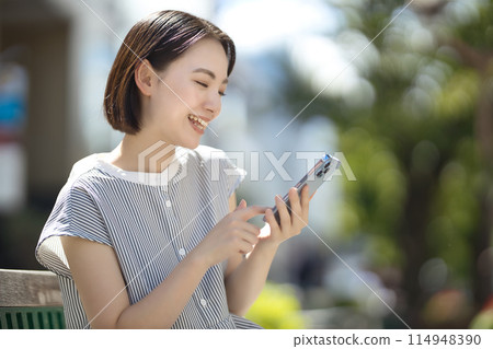 年輕女子坐在城市的長凳上，看著她的智慧型手機 114948390