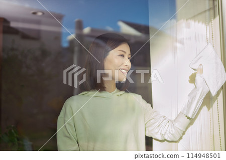 A middle-aged woman wiping windows in the living room 114948501