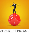 Businessman balancing on a giant red dice 114948688