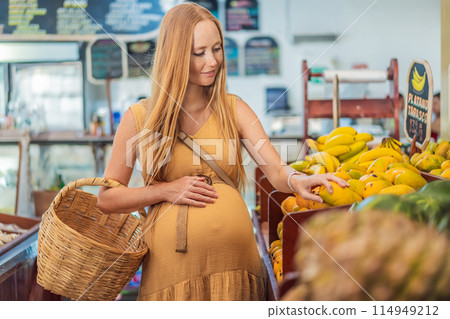 A pregnant woman is at a fruit stand in a grocery store Pregnant woman buying organic vegetables and fruits at Mexican style farmers market A pregnant woman is at a fruit stand in a grocery store Pregnant woman buying organic vegetables and fruits at Mexican style farmers market 114949212