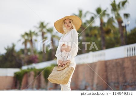 Woman in Elegant Beach Outfit Outdoors Against Palm Trees on the Background During Summer Vacations Woman in Elegant Beach Outfit Outdoors Against Palm Trees on the Background During Summer Vacations 114949352