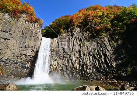 A waterfall with autumn leaves and a rainbow over the pool A waterfall with autumn leaves and a rainbow over the pool 114949756