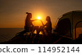 Two female hikers set up camp on a seaside cliff. 114952144