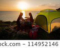 Two female hikers set up camp on a seaside cliff. 114952146