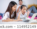 Father and mother with daughter relaxing and using laptop computer on bed. 114952149