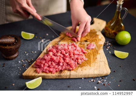 Woman cut tuna steak into slices on a wooden cutting board at domestic kitchen Woman cut tuna steak into slices on a wooden cutting board at domestic kitchen 114952997