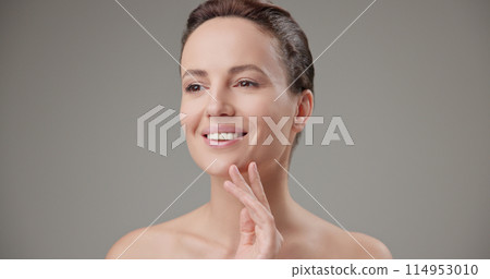 Beauty, health, cosmetics, anti-aging therapy and skin care concept - young beautiful brunette Caucasian woman touching face and looking at camera smiling Beauty, health, cosmetics, anti-aging therapy and skin care concept - young beautiful brunette Caucasian woman touching face and looking at camera smiling 114953010