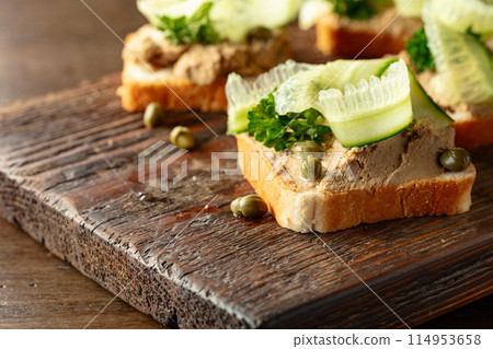 Open sandwiches with pate, cucumber, capers, and parsley on a old cutting board. 114953658