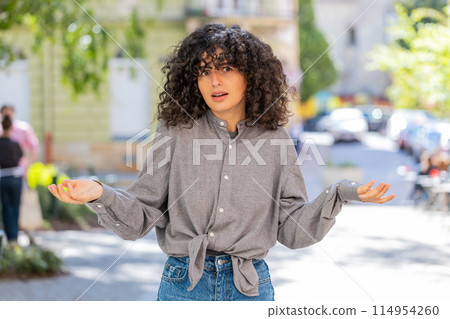 Angry frustrated woman raising hands asking reason of failure demonstrating disbelief irritation 114954260