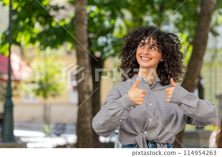 Happy young woman girl showing thumbs up like sign something good positive feedback on city street 114954263
