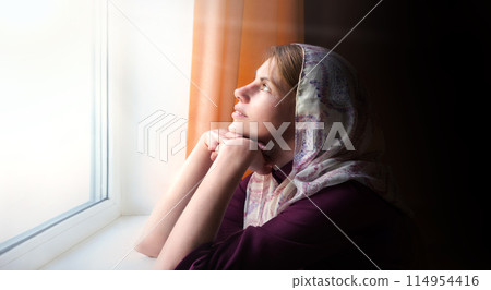 Girl praying by the window Girl praying by the window 114954416