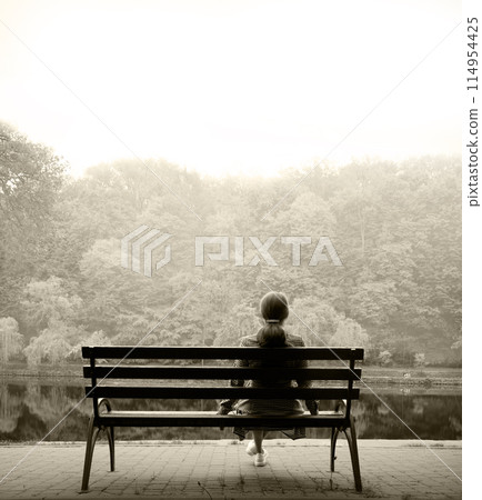 Lonely girl on a bench by the lake Lonely girl on a bench by the lake 114954425