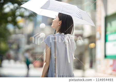A young woman walking through the city with a parasol A young woman walking through the city with a parasol 114954493