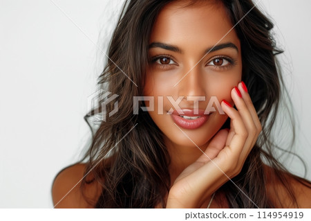 Young woman with dark hair, softly touching her face, showcasing natural beauty and a gentle smile 114954919