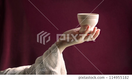 A hand in ancient clothing holds a clay bowl A hand in ancient clothing holds a clay bowl 114955182