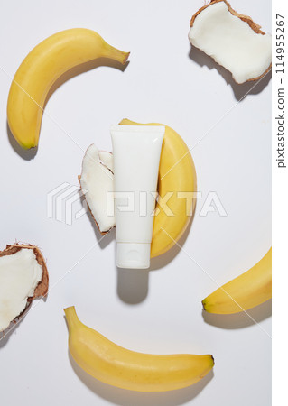 The white unbranded cosmetic tube flat lay on a white counter top, with various pieces of coconut and a bananas lay scattered around. Photo for promotion with overhead view and blank space for design 114955267