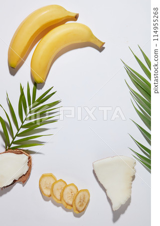 Creative template for design fruit extract products advertising on the white flat, banana, coconut and green leaf placed surrounded a vacant space in center. Presentation space, high angle view 114955268