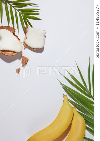 Tropical fruit as banana and coconut featured on white countertop, decorated by fresh green coconut leaves, vacant space in center for displaying product has fruit origin. Top view, copy space Tropical fruit as banana and coconut featured on white countertop, decorated by fresh green coconut leaves, vacant space in center for displaying product has fruit origin. Top view, copy space 114955277