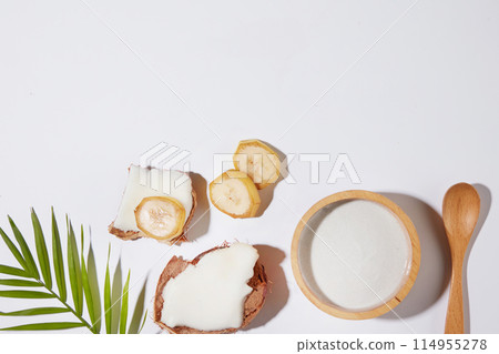 Fruit composition theme photo on white texture, a wooden bowl contains banana coconut extract placed next to a wooden spoon, some slices of banana and coconut. Top view photo with copy space for text Fruit composition theme photo on white texture, a wooden bowl contains banana coconut extract placed next to a wooden spoon, some slices of banana and coconut. Top view photo with copy space for text 114955278