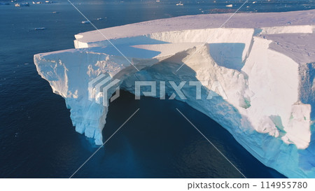 Massive iceberg drifts sunset polar ocean. Giant crashed glacier arch cave in Antarctica. Huge ice wall in pink evening light. Arctic frozen ocean landscape. Travel. Aerial top view drone flight 114955780