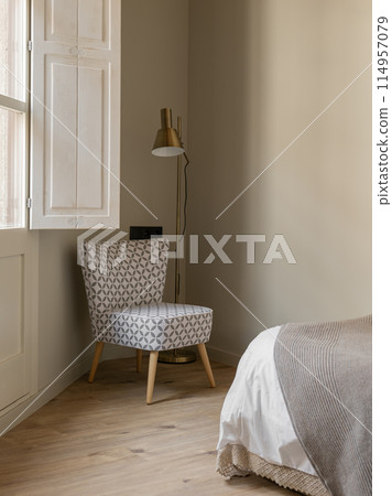 Cozy bedroom corner with patterned chair, modern floor lamp, and neutral tones Cozy bedroom corner with patterned chair, modern floor lamp, and neutral tones 114957079