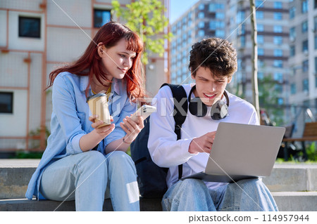 Teenage college students guy and girl talking, sitting outdoor near educational building 114957944