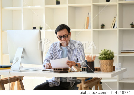 Focused senior architect in eyeglasses working on new project at modern office 114958725