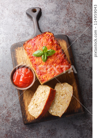 Tasty homemade ground baked chicken meatloaf glazed with ketchup closeup on the wooden board. Vertical top view 114959043