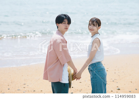 A young couple walking along the beach 114959083
