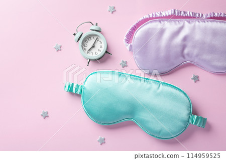 Sleep mask and alarm clock with stars on pastel pink background, top view, copy space 114959525