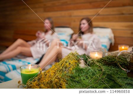 Two women relaxing in a sauna surrounded by candles and herbs Two women relaxing in a sauna surrounded by candles and herbs 114960858