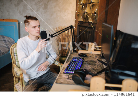 Young man makes a podcast audio recording at home. Man using pc and two professional microphones. Person recording a podcast at home using microphone and computers. Recording online podcast Young man makes a podcast audio recording at home. Man using pc and two professional microphones. Person recording a podcast at home using microphone and computers. Recording online podcast 114961641