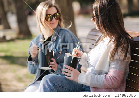 Female friends buy asian food. Girls open boxes and use food sticks. Takeaway food concept 114962399