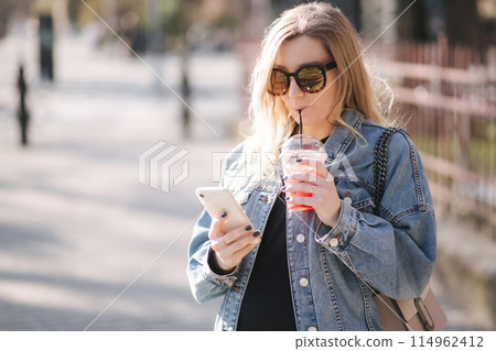 Pretty pregnant woman drinking strawberry lemonade while walking outdoors. Portrait of attractive female in sunglasses using phone Pretty pregnant woman drinking strawberry lemonade while walking outdoors. Portrait of attractive female in sunglasses using phone 114962412