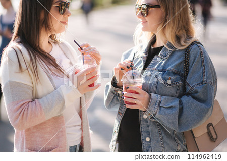 Two female friend drink raspberry lemonade and speak. Happy woman walking outdoors 114962419