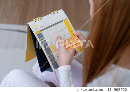 Woman holding birth control pills and checking calendar. Concept of contraception and family planning 114962760