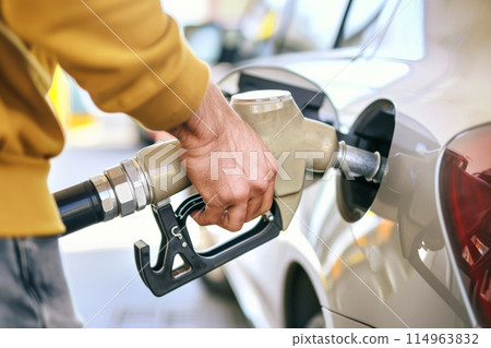 At a gas station, a person in a yellow jacket is fueling up a car using a fuel nozzle 114963832