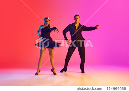 Dynamic shot of young man and woman dancing Zumba in motion in neon lighting against vibrant gradient background. 114964066