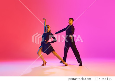 Ballroom dancers, man and woman in stage costumes gracefully performing in neon lighting against vibrant gradient background. 114964140