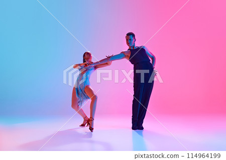 Ballroom dancers, man and woman in fashion stage costumes strike graceful pose in neon lighting against gradient background. 114964199