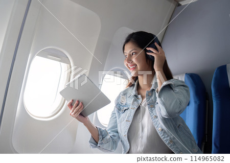 Asian woman using tablet and headphones on airplane during flight Asian woman using tablet and headphones on airplane during flight 114965082