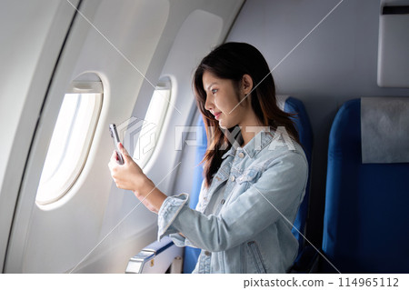 Asian woman taking photo out airplane window during flight 114965112