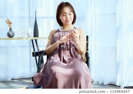 A woman sitting on a chair in a room and looking at her smartphone 114968847