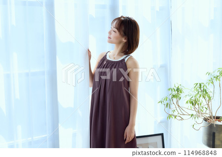 A woman relaxing in a room through lace curtains A woman relaxing in a room through lace curtains 114968848