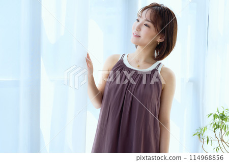 A woman relaxing in a room through lace curtains A woman relaxing in a room through lace curtains 114968856