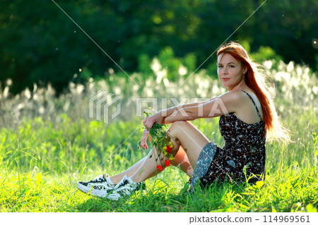 A girl with wild poppies enjoys the view from a hill near the river. Joy, happiness, serenity. Wild poppies by the river. 114969561