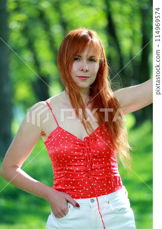 A girl in a red blouse and white jeans poses for the camera in nature. Joy, happiness, serenity. A girl poses for a photographer in nature. A girl in a red blouse and white jeans poses for the camera in nature. Joy, happiness, serenity. A girl poses for a photographer in nature. 114969574