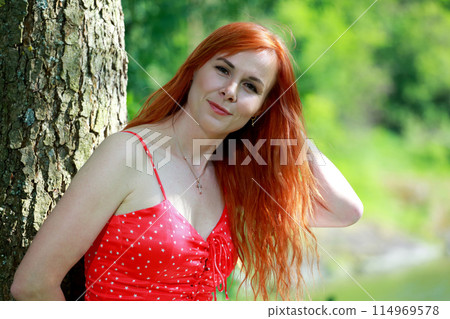 A girl in a red blouse and white jeans poses for the camera in nature. Joy, happiness, serenity. A girl poses for a photographer in nature. 114969578