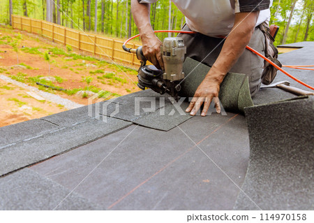 Installation of new asphalt bitumen shingles using an air pneumatic nail gun by roofer Installation of new asphalt bitumen shingles using an air pneumatic nail gun by roofer 114970158