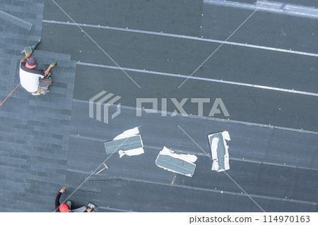 Professional roofing contractor installing new asphalt bitumen shingles on house using an air nail gun Professional roofing contractor installing new asphalt bitumen shingles on house using an air nail gun 114970163
